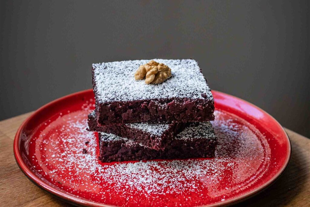 Rote-Bete-Brownies mit Puderzucker und Walnuss auf rotem Teller