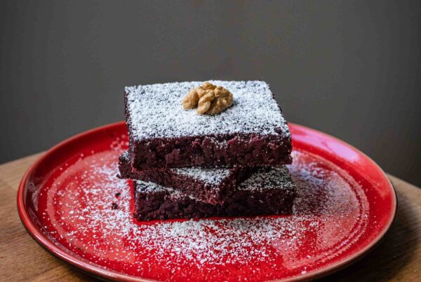 Rote-Bete-Brownies mit Puderzucker und Walnuss auf rotem Teller